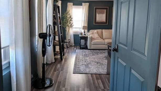 A living room with a blue door, a white sofa, a fan, and a rug.
