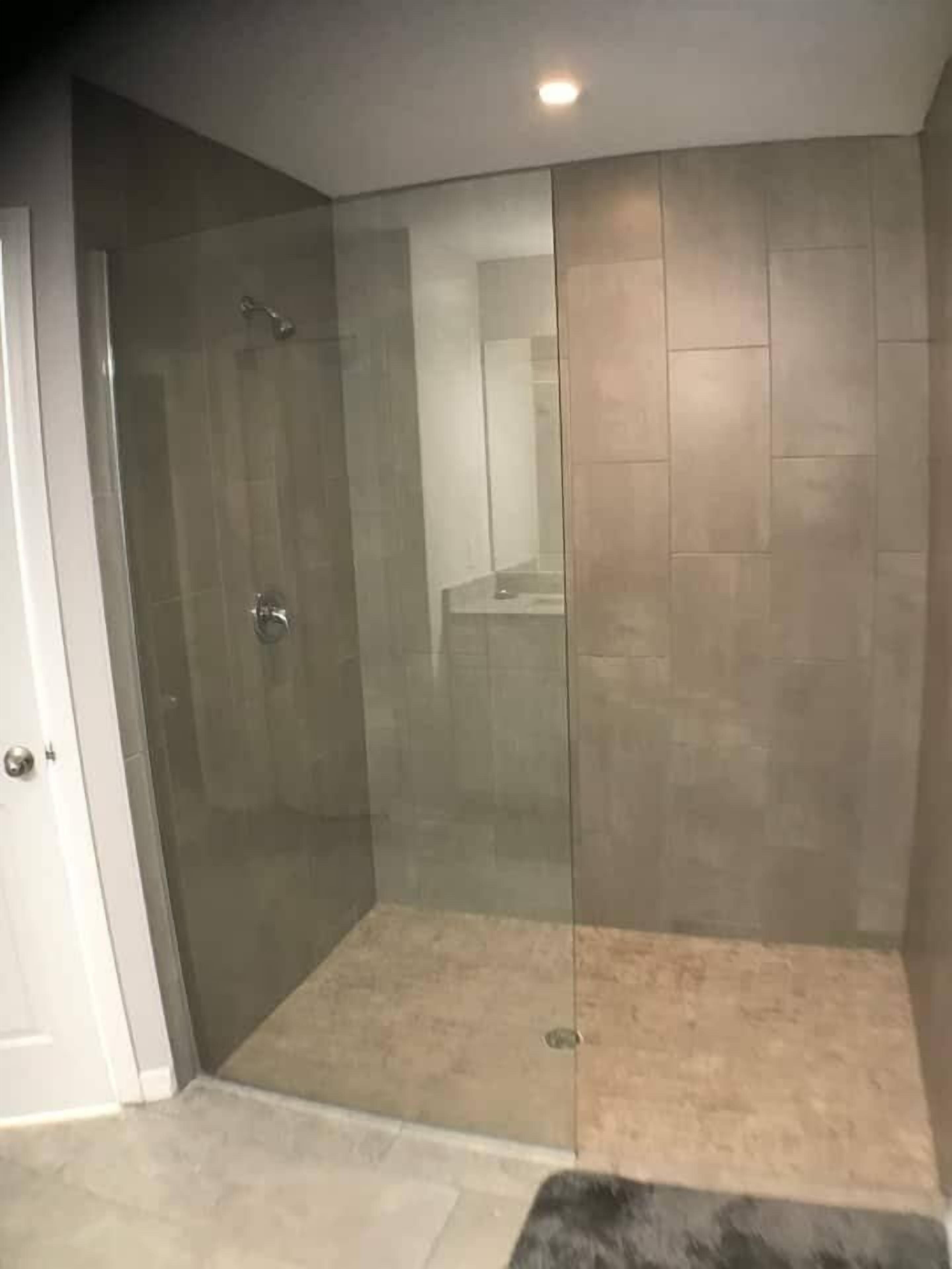 Un baño moderno con ducha envuelta en vidrio, paredes con azulejos y una paleta de colores neutros.