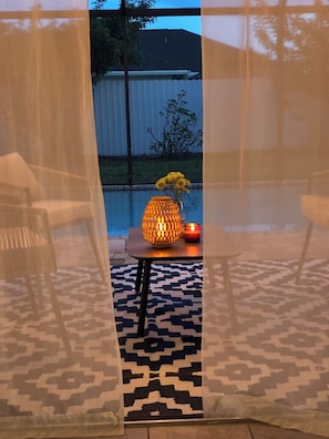 Uma área externa com assentos, um tapete estampado, uma mesa com um lanterna decorativa e uma cadeira.