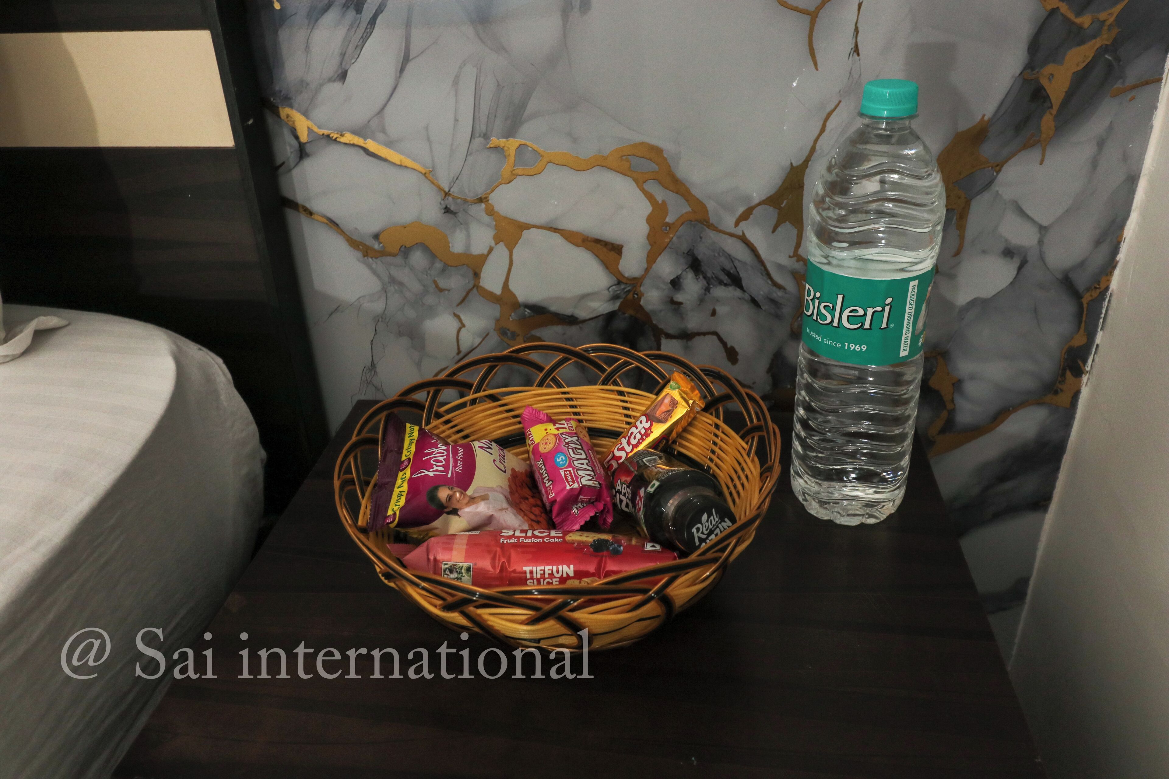 A bed, a water bottle, and a basket with snacks on a table with a marble-patterned wall.