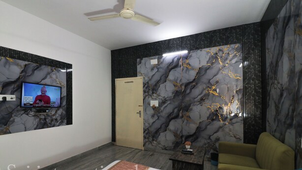 A modern hotel room with a flat-screen TV mounted on the wall, a ceiling fan, a bed with a neatly made bedspread, and a seating area with a sofa and armchair. - Sai International (Bidhannagar)
