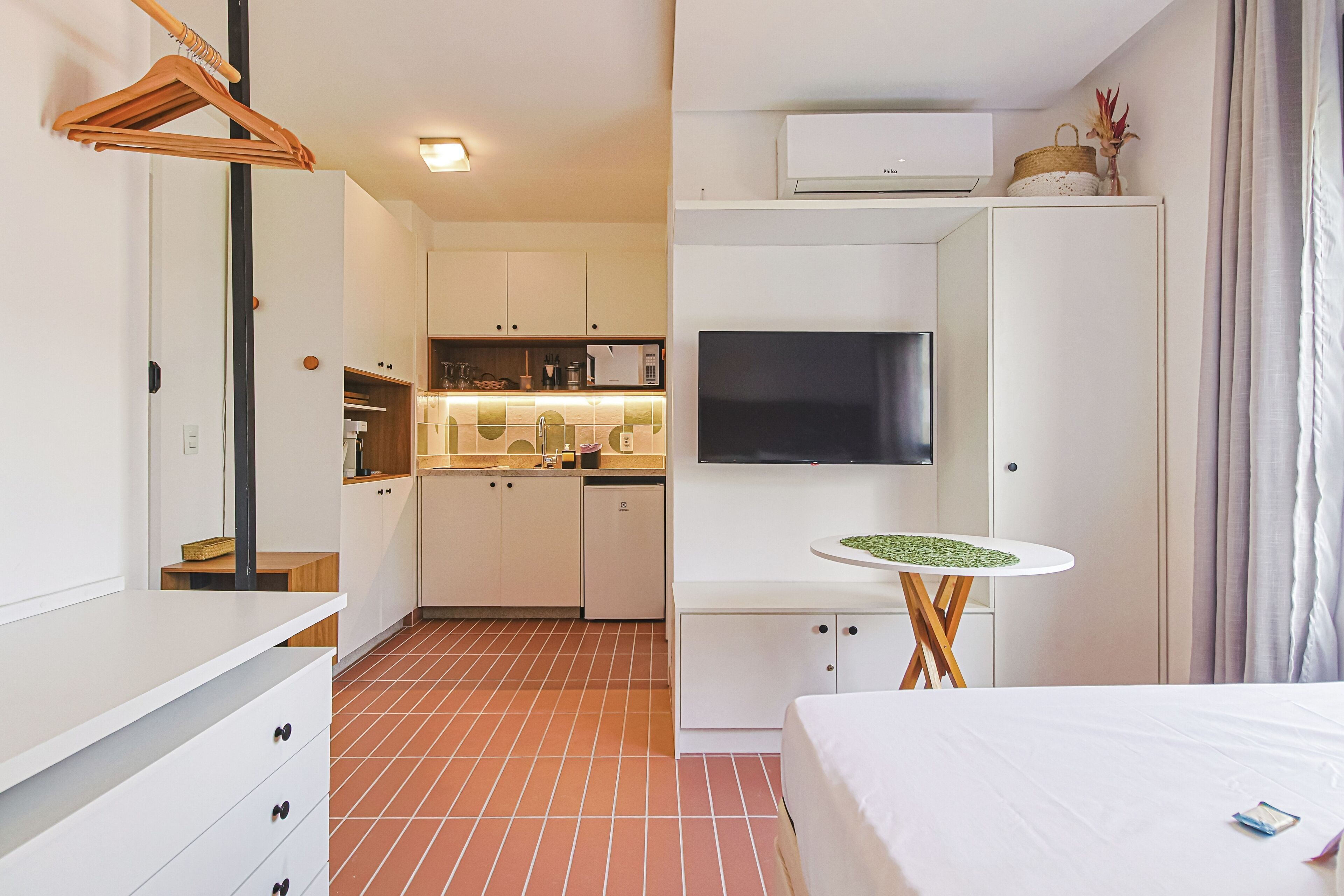 A modern hotel room with a bed, a small table, a TV, and a kitchenette.