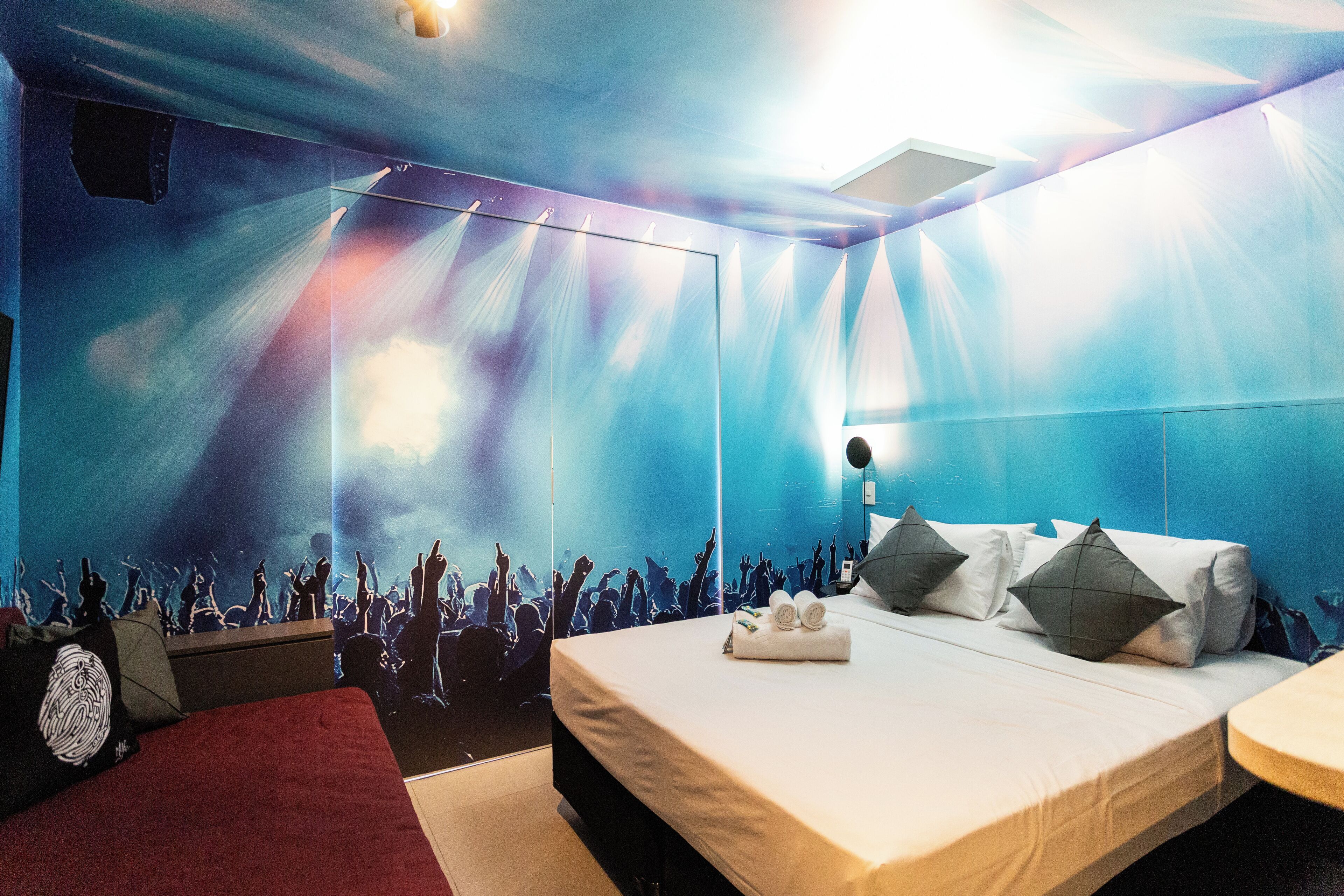 A hotel room with a large bed, a red sofa, and a wall mural of a concert.