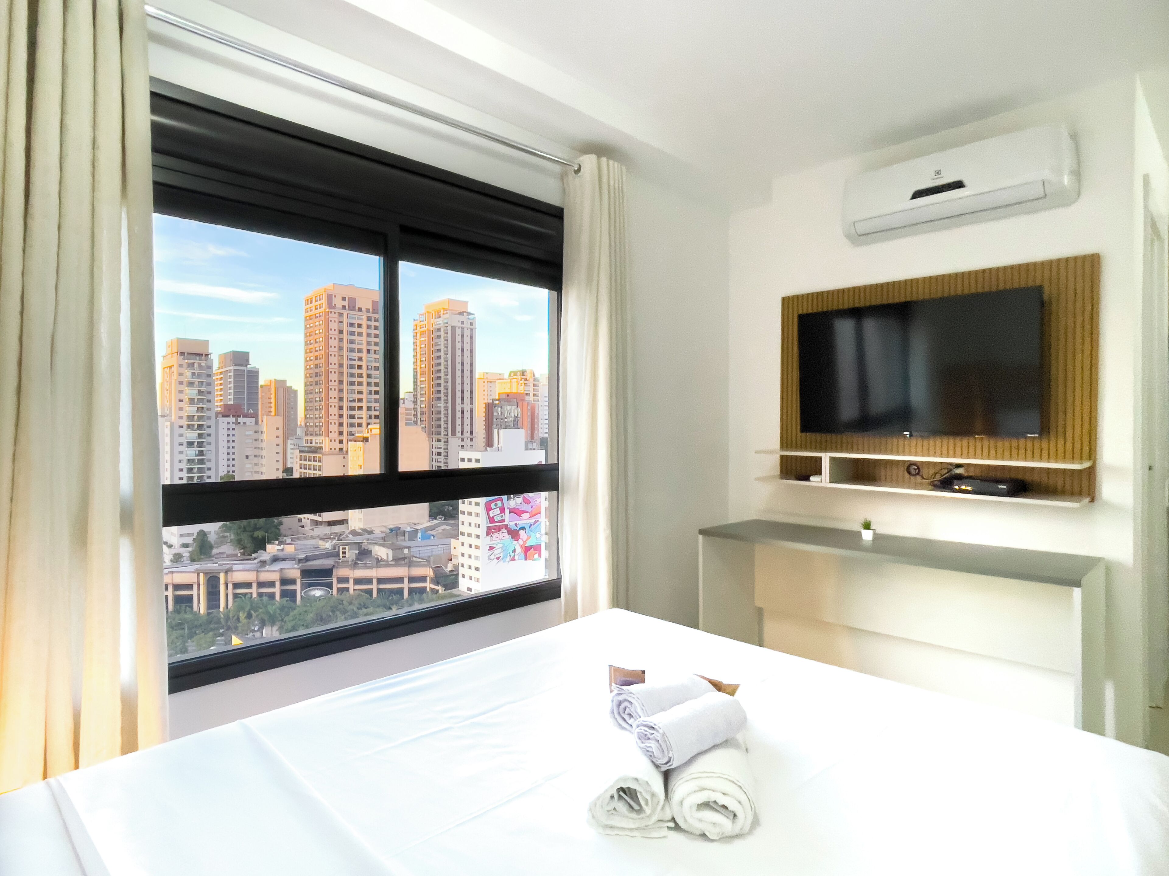 Habitación de hotel con cama, televisión montada en la pared y ventana con vistas a la ciudad.
