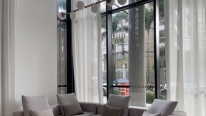 A modern living room with a grey sectional sofa, sheer white curtains, and a view of the street outside. - Lira Perdizes (Sao Paulo)