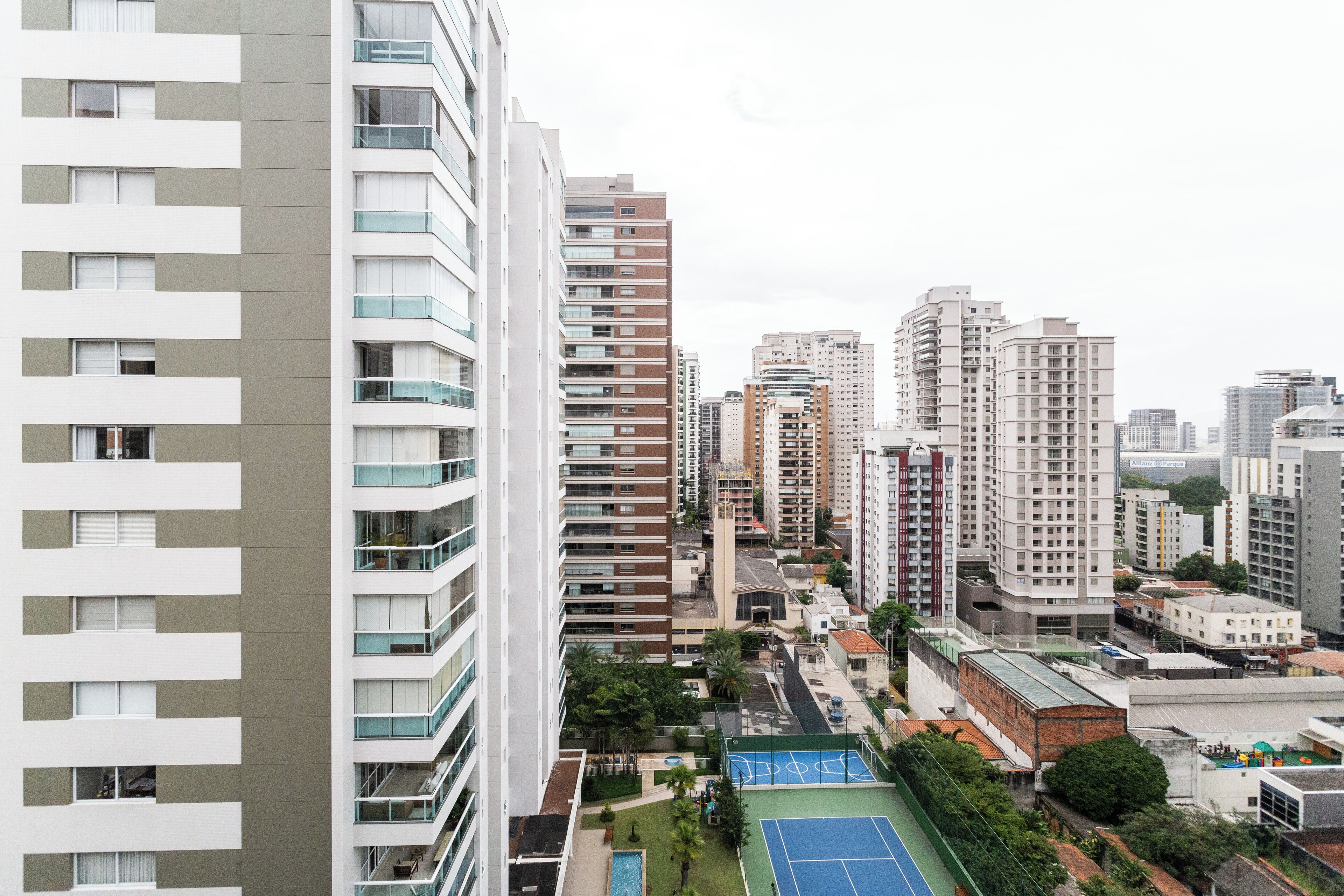 Un immeuble de grande hauteur doté de nombreux balcons, d’un court de tennis et entouré d’autres bâtiments urbains.
