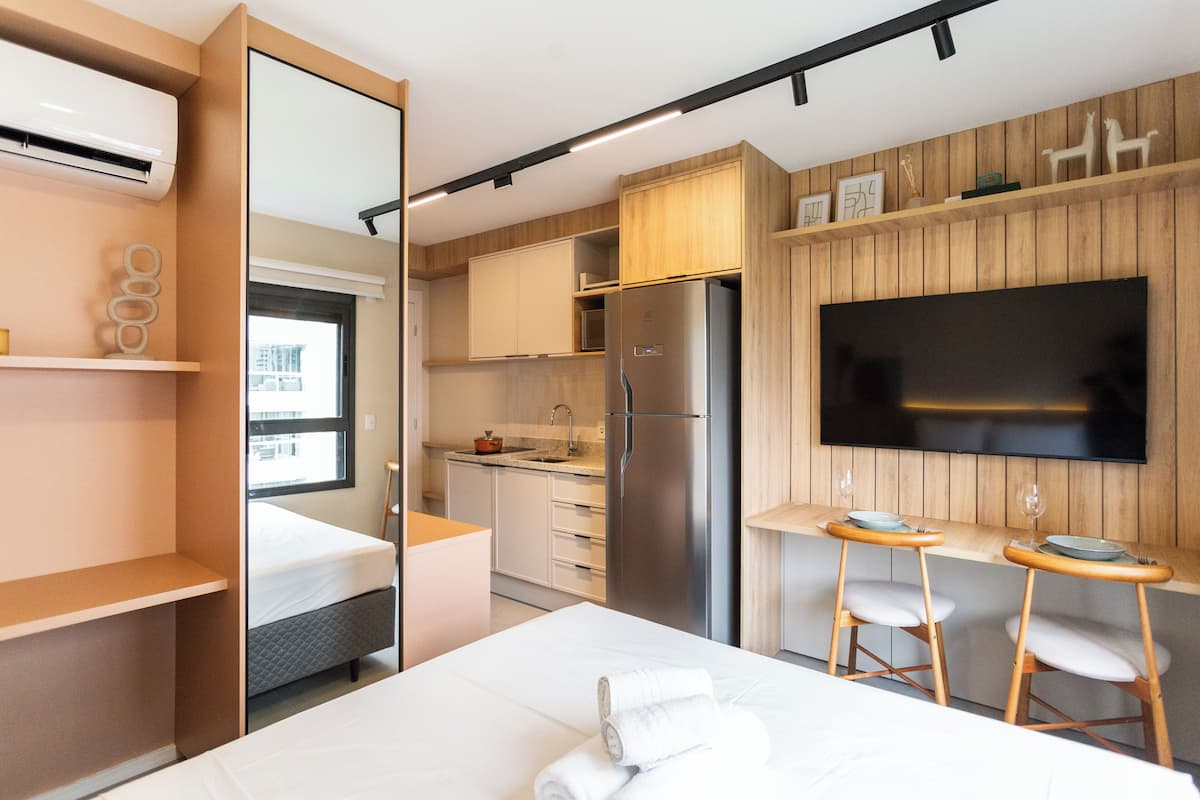 A modern hotel room with a bed, a kitchenette, a TV, and a bathroom.