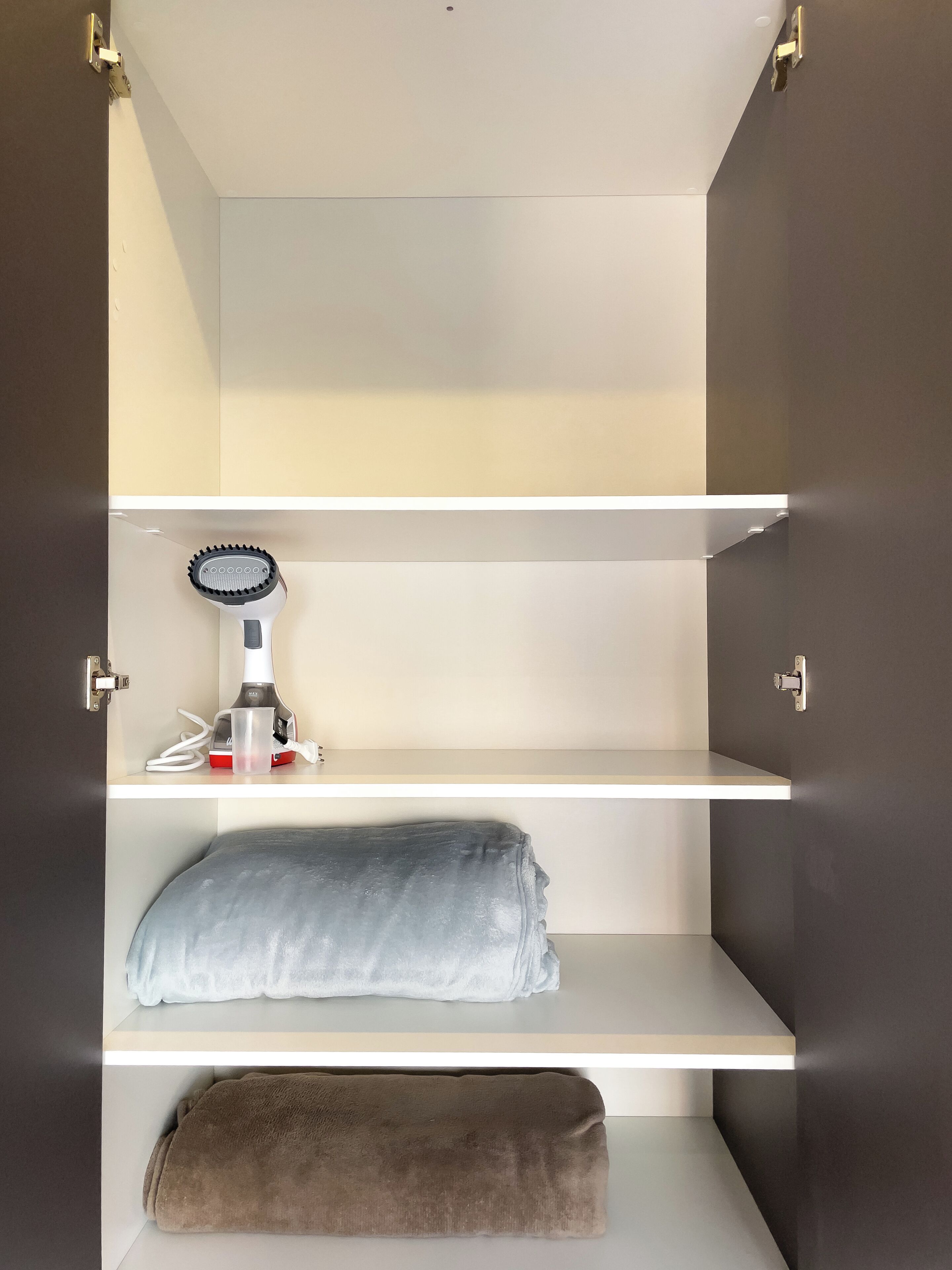A closet with three shelves, a hairdryer, and a towel.
