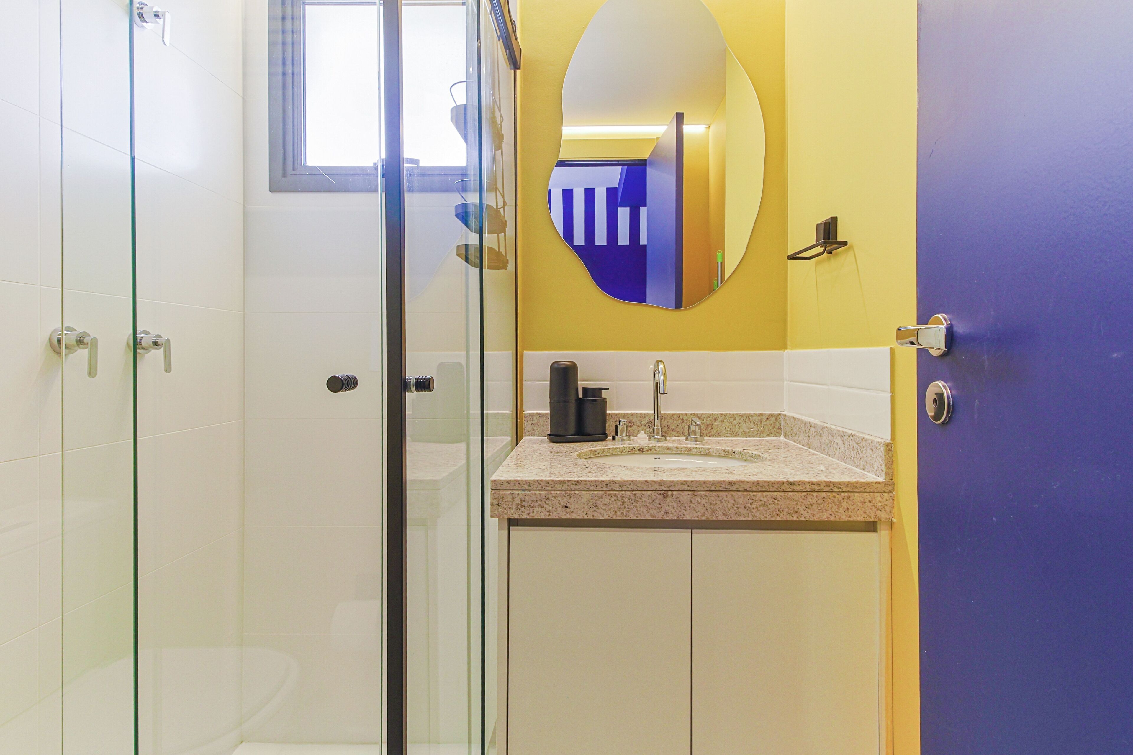 A bathroom with a glass shower enclosure, a sink with a mirror above it, and a door with a handle.