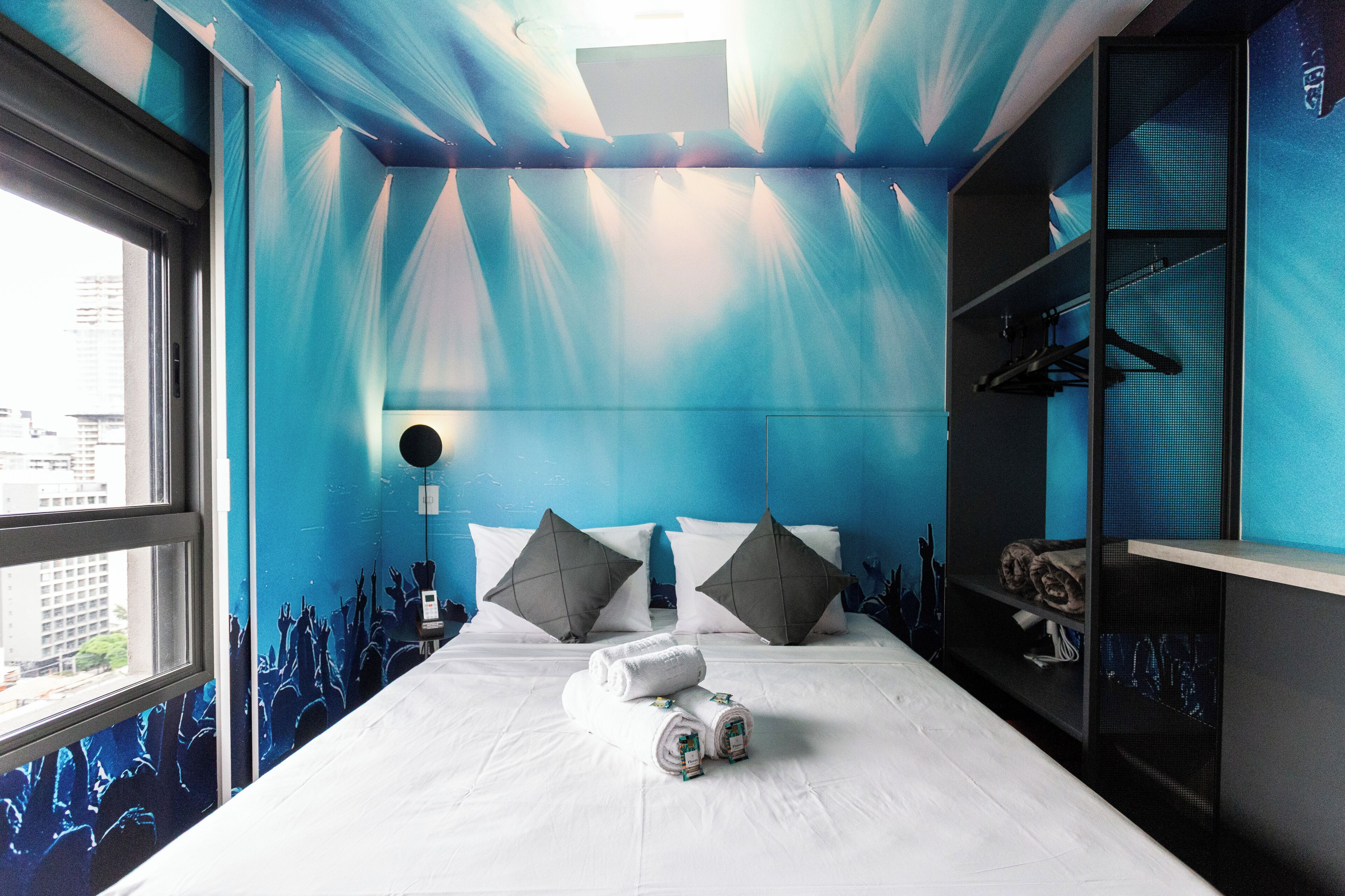 Une chambre d’hôtel avec un lit, des oreillers, une table de chevet, une armoire et une fenêtre.
