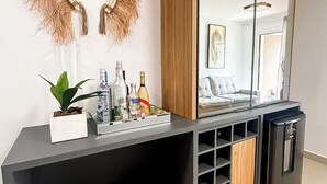 A modern room with a large mirror, a minibar, two stools, and a decorative wall piece. - Apartment on the sand in the South beaches (Ilheus)