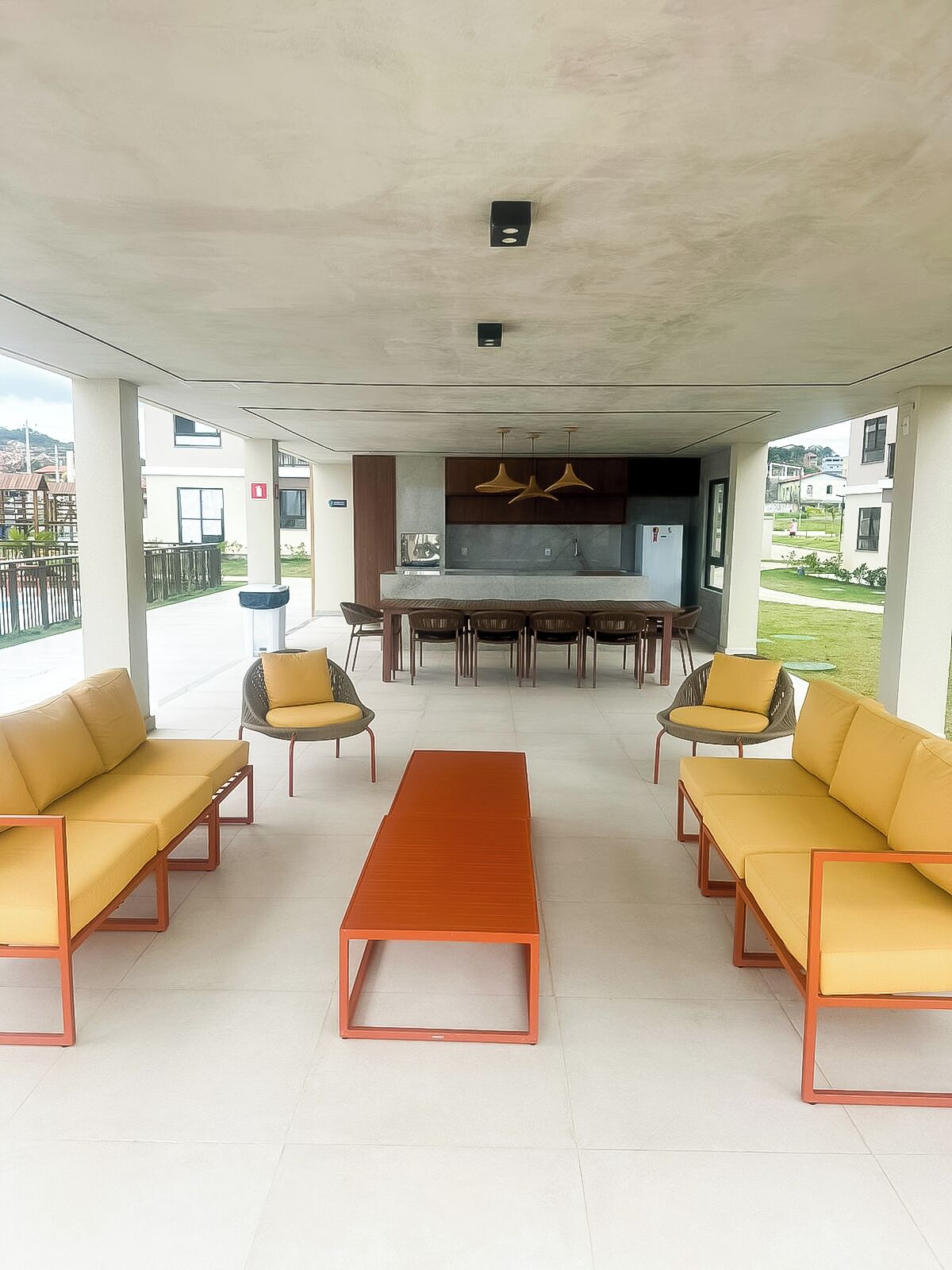 A modern outdoor seating area with sofas and chairs, a central table, and a kitchen area with hanging lights.