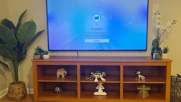 A television on a wooden stand with decorative items and a large plant beside it.