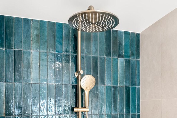 A showerhead with a round, perforated head and a gold-colored handle, mounted on a vertical rod. - Beachfront W/ Breathtaking Views (Blackmans Bay)