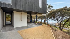 A modern house with a concrete patio, a small seating area with a table and chairs, and a view of the sea. - Beachfront W/ Breathtaking Views (Blackmans Bay)