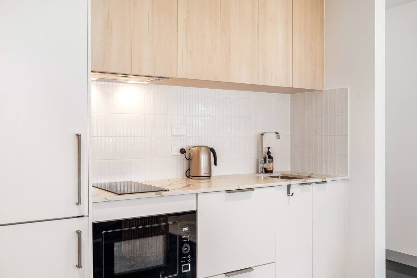A modern kitchen with white cabinets, a stainless steel kettle, a sink, and a built-in oven.