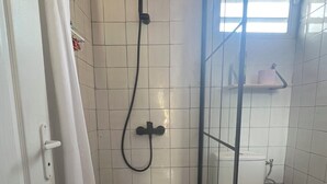 A small bathroom with a shower, toilet, and a window.