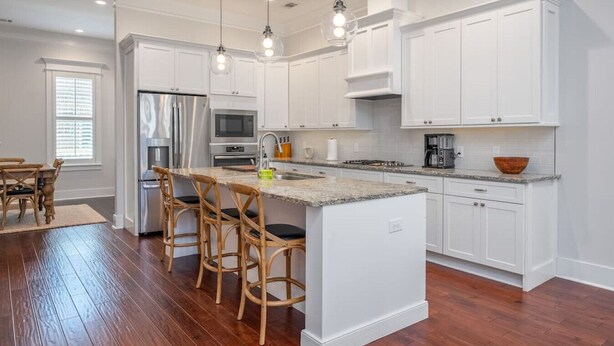 A modern kitchen with white cabinetry, a central island with bar stools, stainless steel appliances, and pendant lighting. - Rose House - 2 Primary Suites, Easy Parking (Savannah)