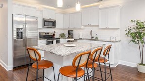 Une cuisine moderne avec des meubles blancs, des appareils en acier inoxydable et un îlot en granit doté de tabourets de bar.
