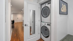 Une buanderie équipée de deux machines à laver à chargement frontal superposées, une porte donnant sur une autre pièce et une œuvre d’art représentant un cygne, encadrée, accrochée au mur.
