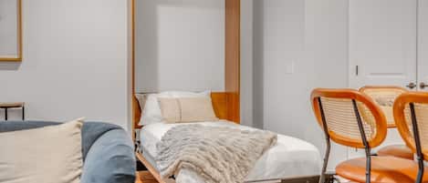 Une chambre à coucher de taille modeste, comprenant un lit, une tête de lit en bois, une petite table et deux chaises.