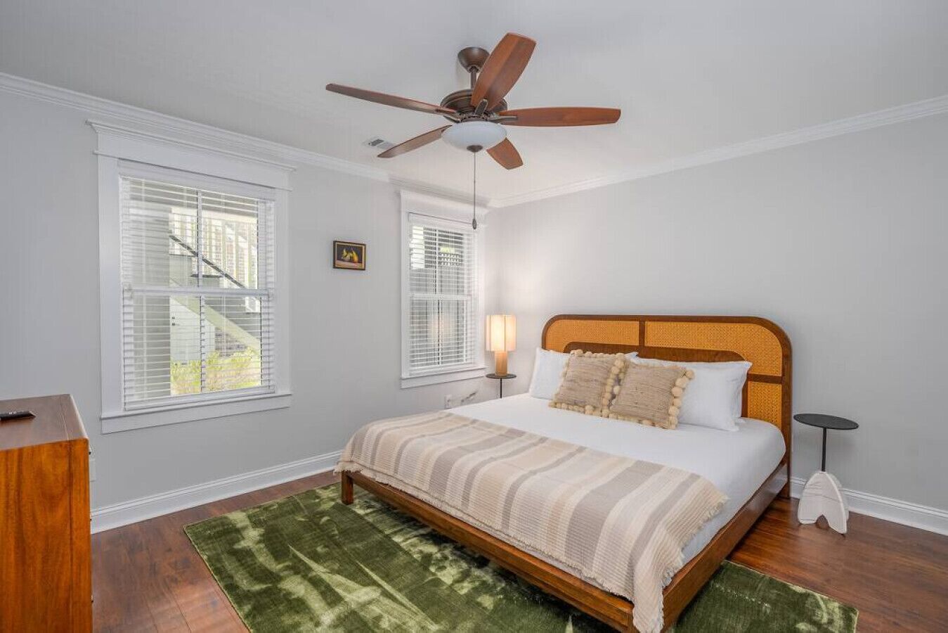 Une chambre avec un lit en bois, un ventilateur de plafond et un tapis vert.