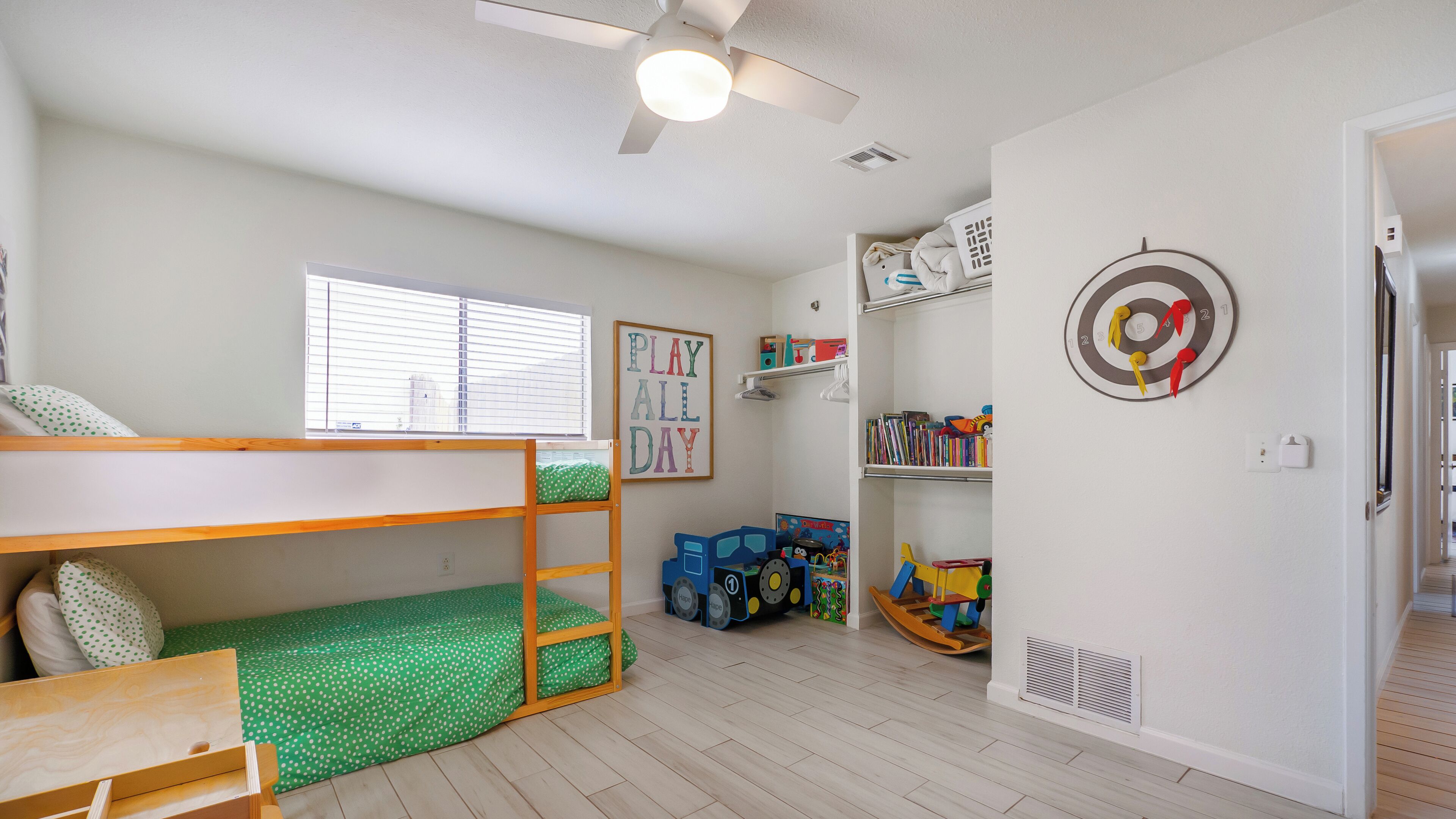 A child's bedroom with bunk beds, a ceiling fan, a bookshelf, and a target wall decoration.