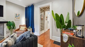 Un salon avec un canapé, une table basse et un téléviseur. Une porte donne accès à une autre pièce dont l’un des murs est décoré d’un motif.