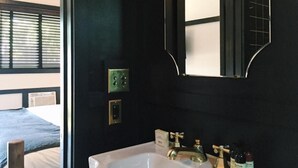 A bathroom with a white sink, a mirror, and a window with blinds.
