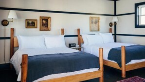 A double room with two wooden beds, white bedding, and a red patterned rug.