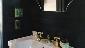 A bathroom with a white sink, gold faucets, and a mirror with a black frame. There are three bottles of toiletries on the sink.