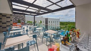 Un espace de restauration en plein air avec des tables et des chaises, un bar avec des bouteilles et des verres, et une vue sur le paysage.