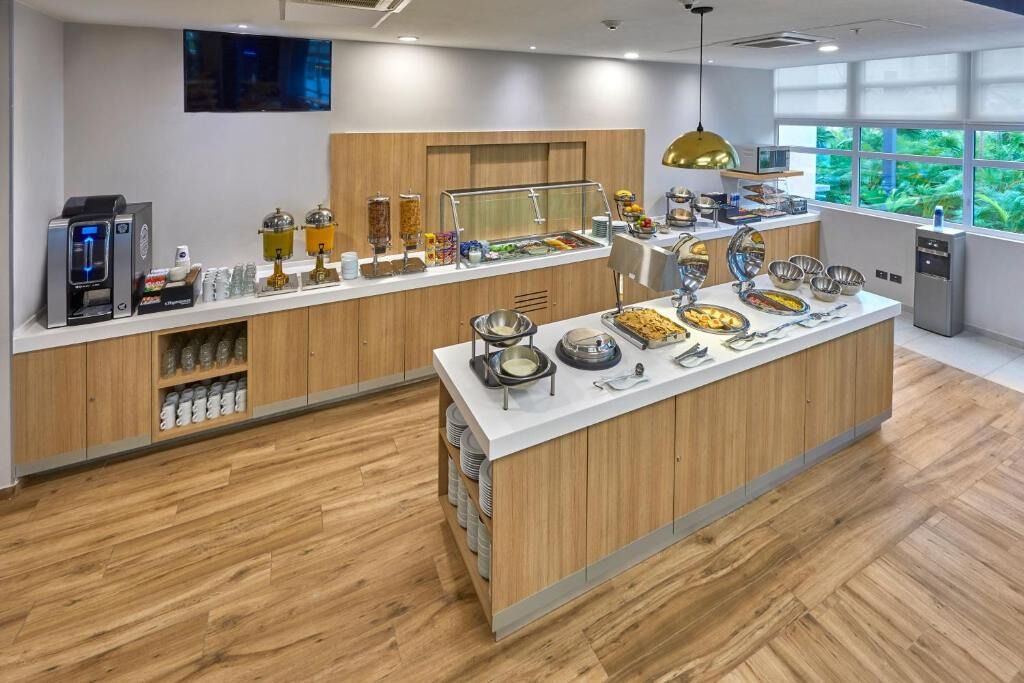 A modern breakfast bar with a variety of food options, a coffee machine, and a view of greenery through large windows.