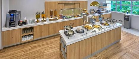 A modern breakfast bar with a variety of food options, a coffee machine, and a view of greenery through large windows.