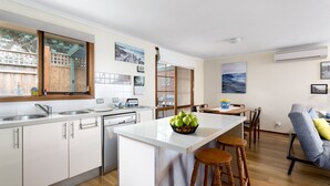 Een moderne keuken met witte kasten, een centraal eiland met barkrukken, een eetgedeelte met tafel en stoelen, en kunstwerken aan de wanden.