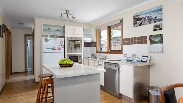 Een moderne keuken met een centraal eiland, roestvrijstalen apparatuur en uitzicht op het groen door een raam.