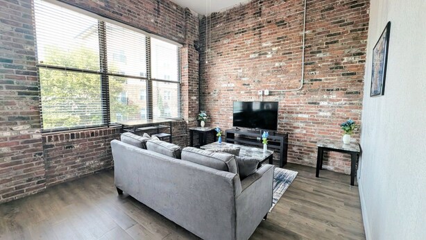 A living room with a brick wall, a gray sofa, a TV, and a ceiling fan.