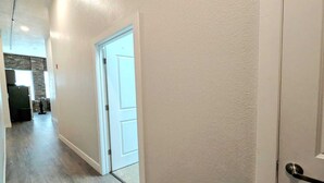 A hallway with a white door, wooden flooring, and a textured wall.