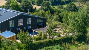 A modern house with a large deck, surrounded by lush greenery and hills.