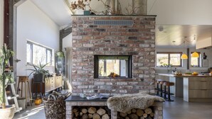 A modern kitchen with a brick fireplace, wooden bar stools, and a large window.