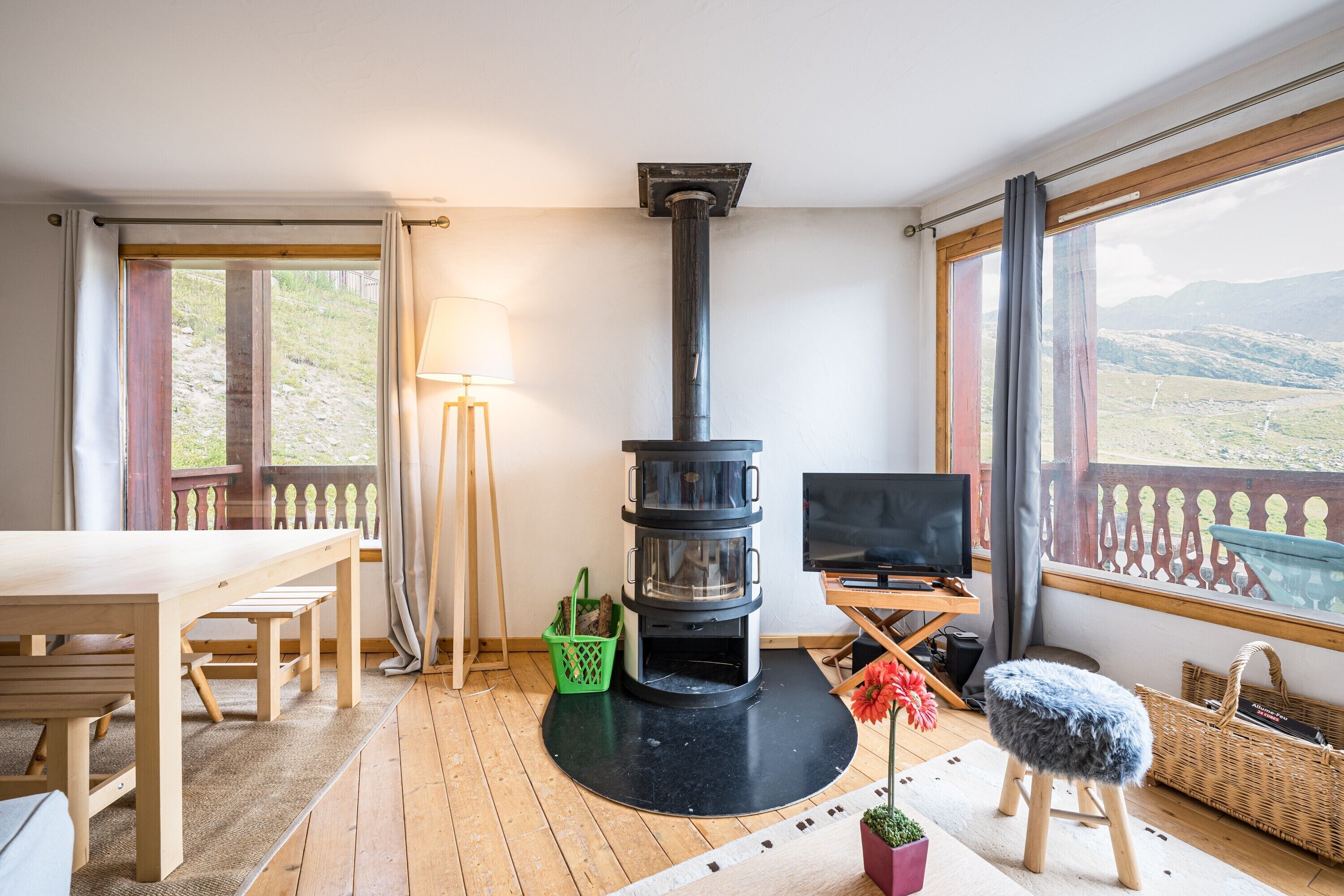 A cozy room with a fireplace, wooden furniture, a TV, and large windows with a view.