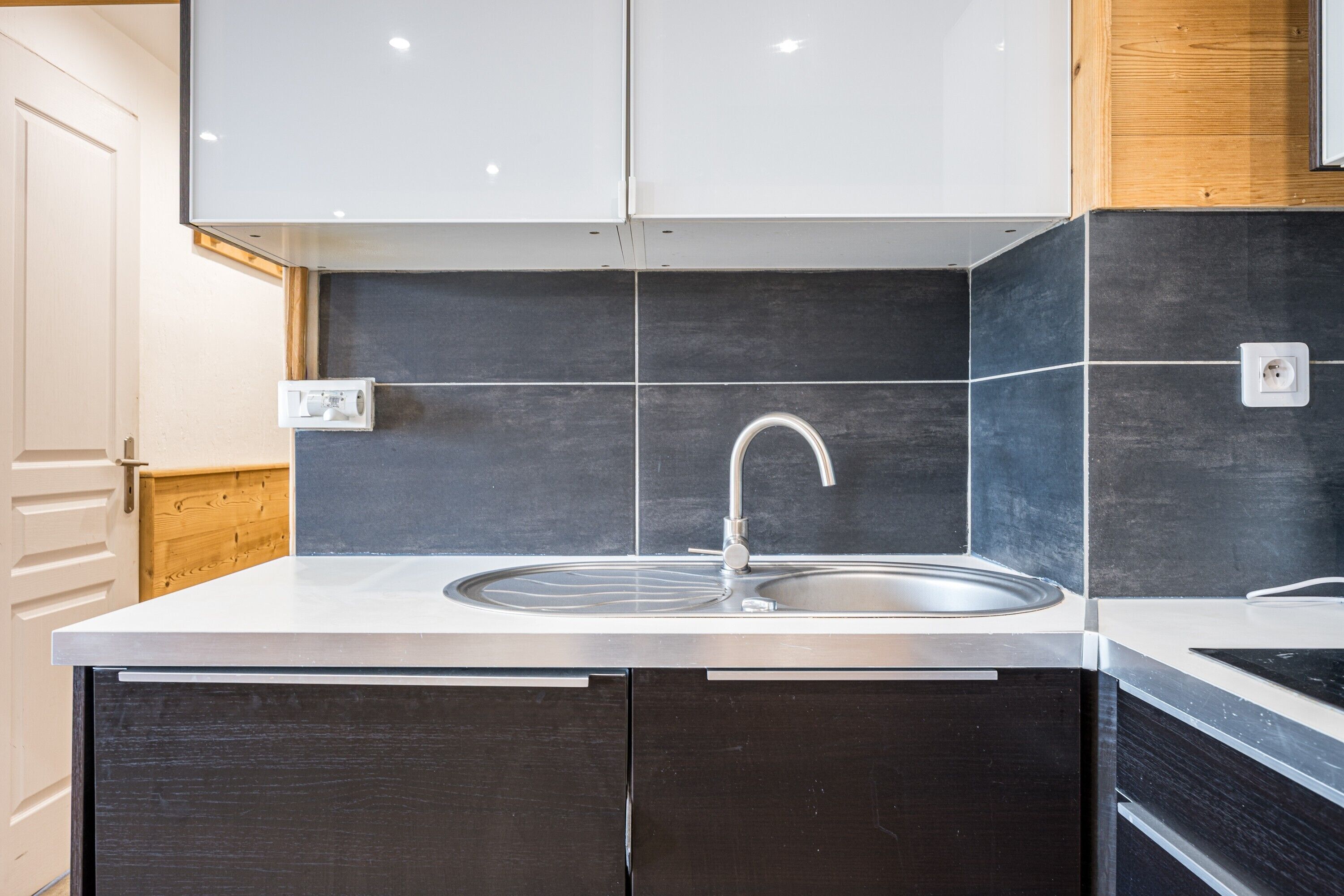 Een moderne keuken met een roestvrijstalen spoelbak, een donkere betegelde spatwand en houten kastjes.
