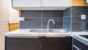 Una cocina moderna con un lavamanos de acero inoxidable, salpicadero de baldosas oscuras y armarios de madera.