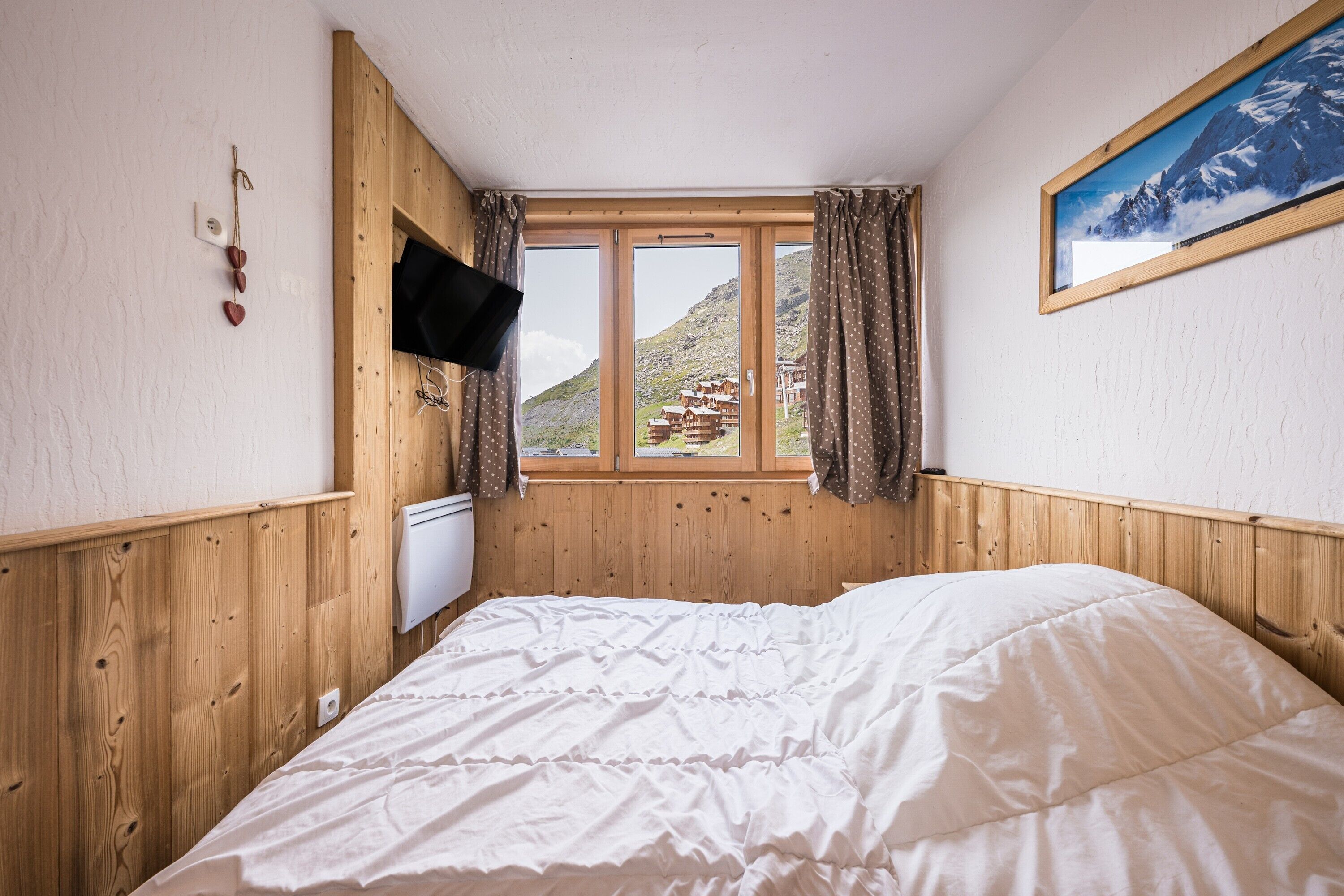 Een slaapkamer met een houten lambrisering, een bed met wit beddengoed, een raam met gordijnen en een schilderij aan de muur.