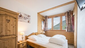 Una cama de madera con ropa de cama blanca, una mesita de noche con lámpara y un armario con un recorte en forma de corazón.
