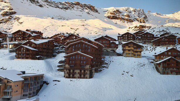 Un conjunto de cabañas de madera con balcones, al pie de una montaña nevada.