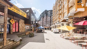 Calle con tiendas, mesas al aire libre y una carpa azul.