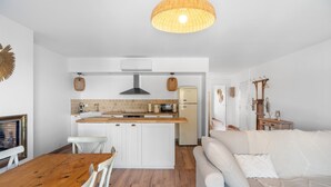 Une cuisine compacte avec des meubles blancs, une table à manger en bois et un canapé blanc.