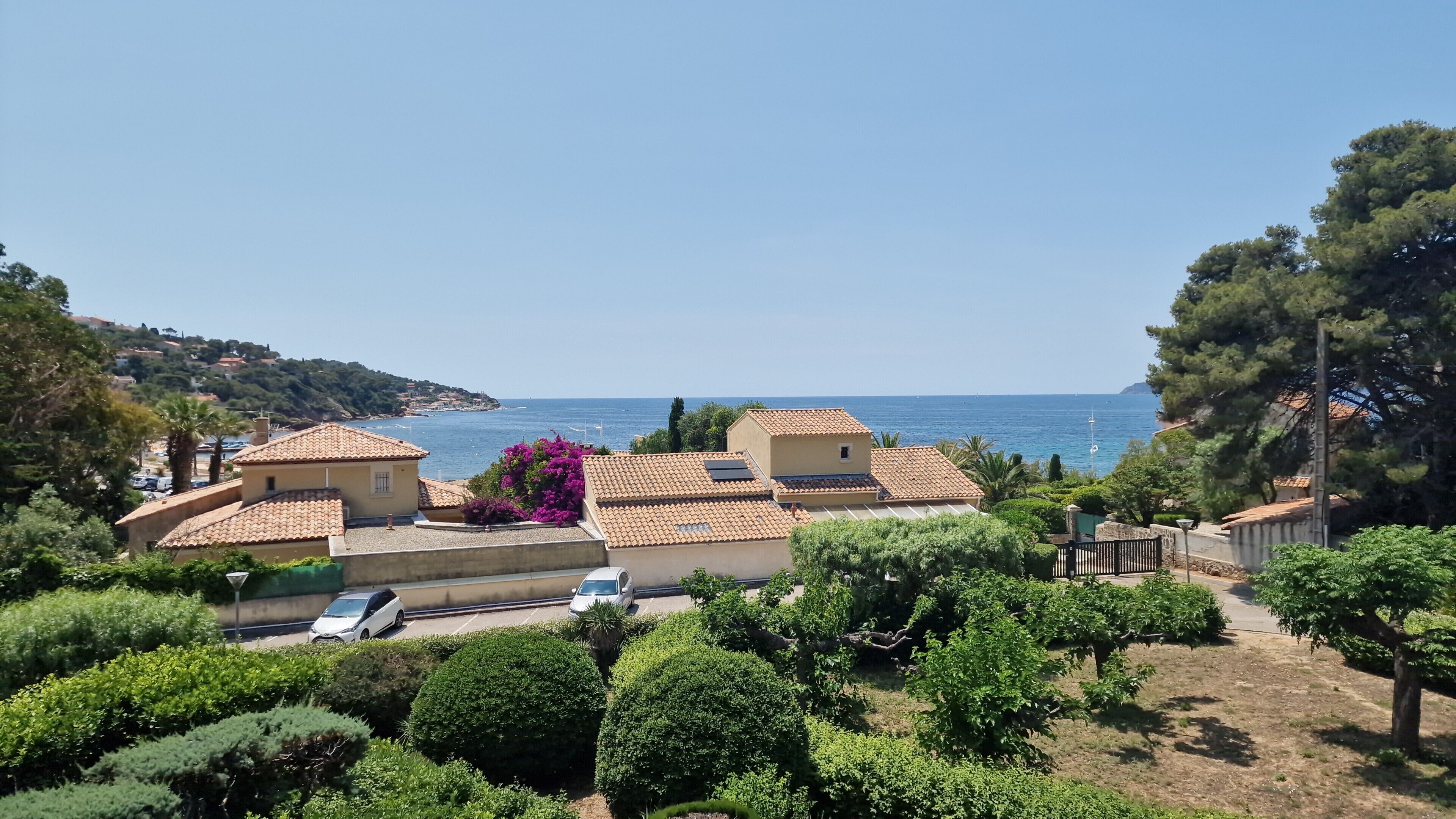 A coastal residential area with houses, a clear sky, and the sea in the background.