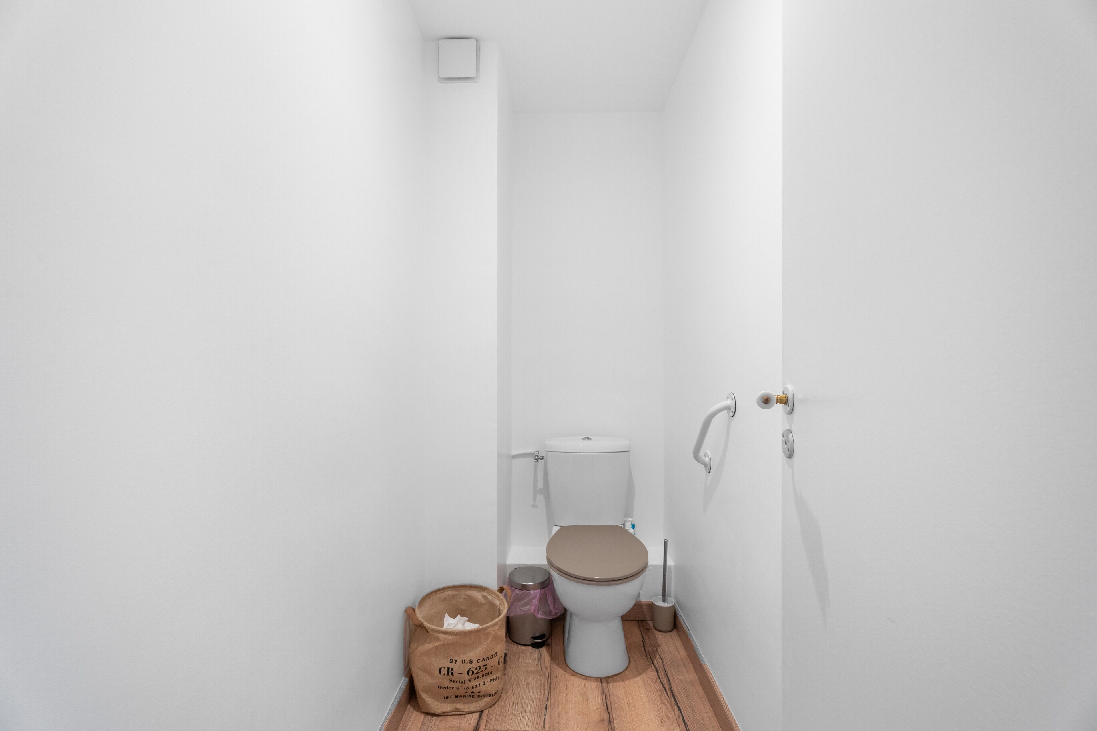 Un baño pequeño con paredes blancas, un inodoro, un cubo de basura y un paquete de pañuelos.